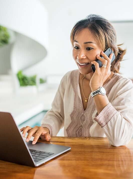 woman talking on the phone while looking at her laptop