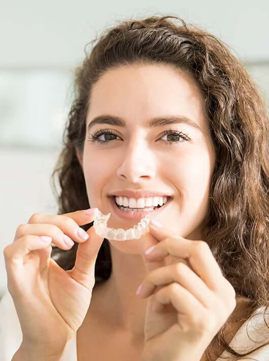 woman inserting clear aligners onto her teeth